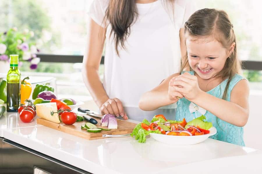 Cute little girl cooking with her mother. Healthy food, cooking healthy salad with vegetables ingredients. Mom and daughter cooking together. Recipe food for baby or child