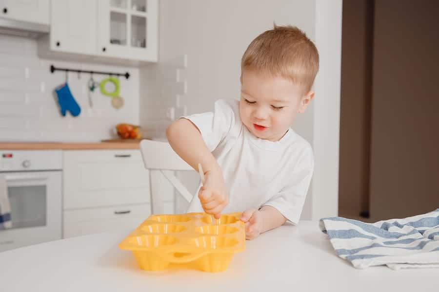 Young family cooking in kitchen. Happy child boy laughing, smiling, oiling baking dish for cupcakes. Concept team work. Learning While You Cook
