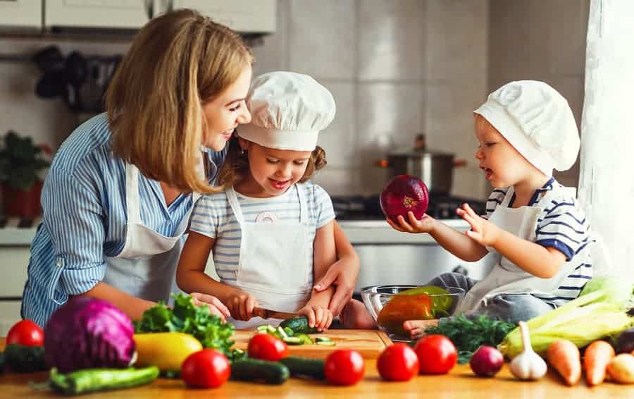 Healthy eating. Happy family mother and children prepares vegetable salad in kitchen. Learning While You Cook