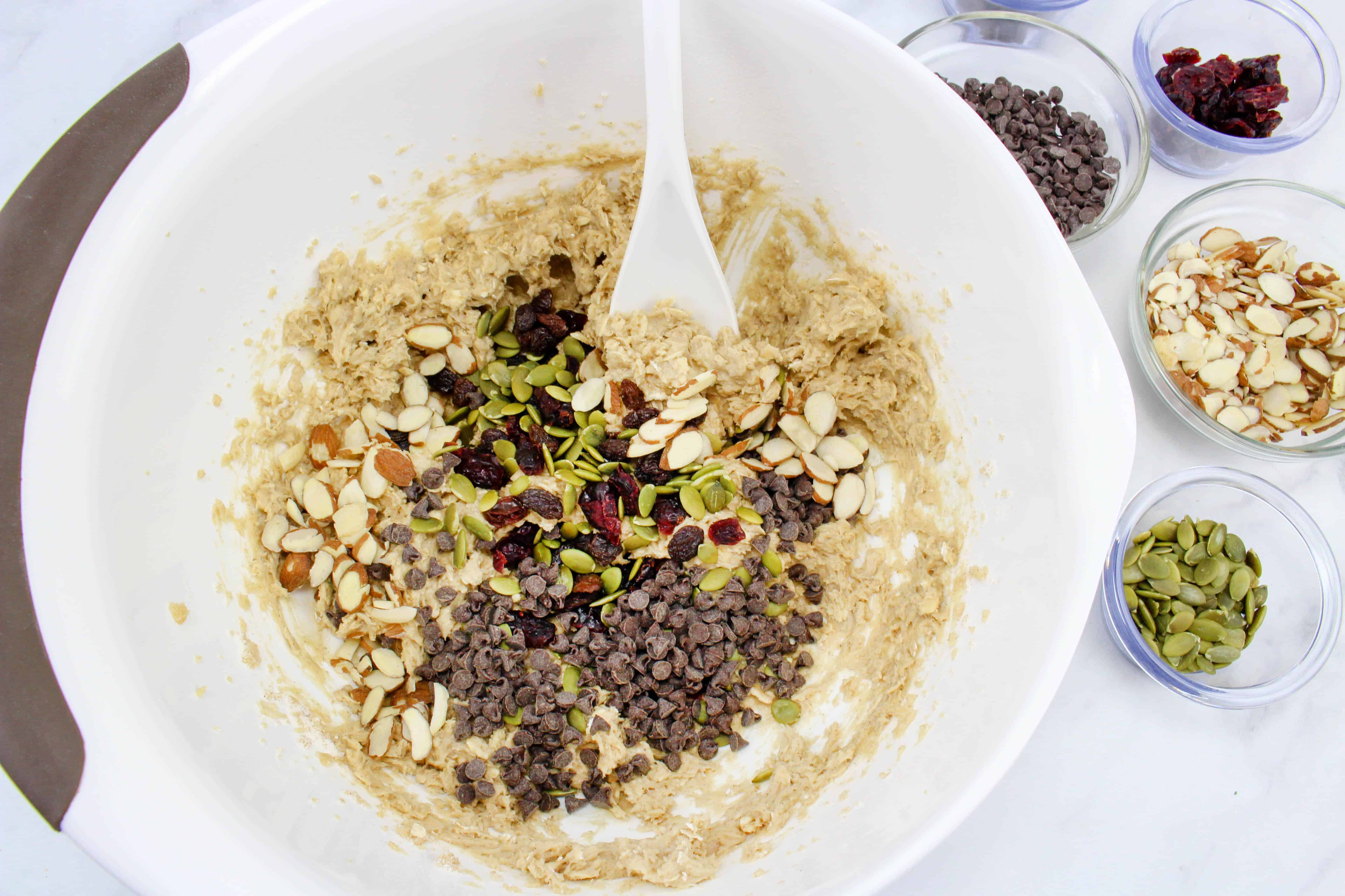 Mixing cranberries, chocolate chips, almonds, pumpkin seeds, and raisins to the trail mix cookies mixture.