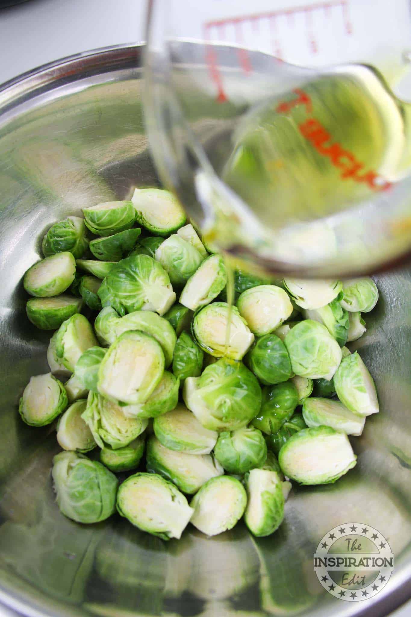 Olive oil being poured over brussels sprouts.