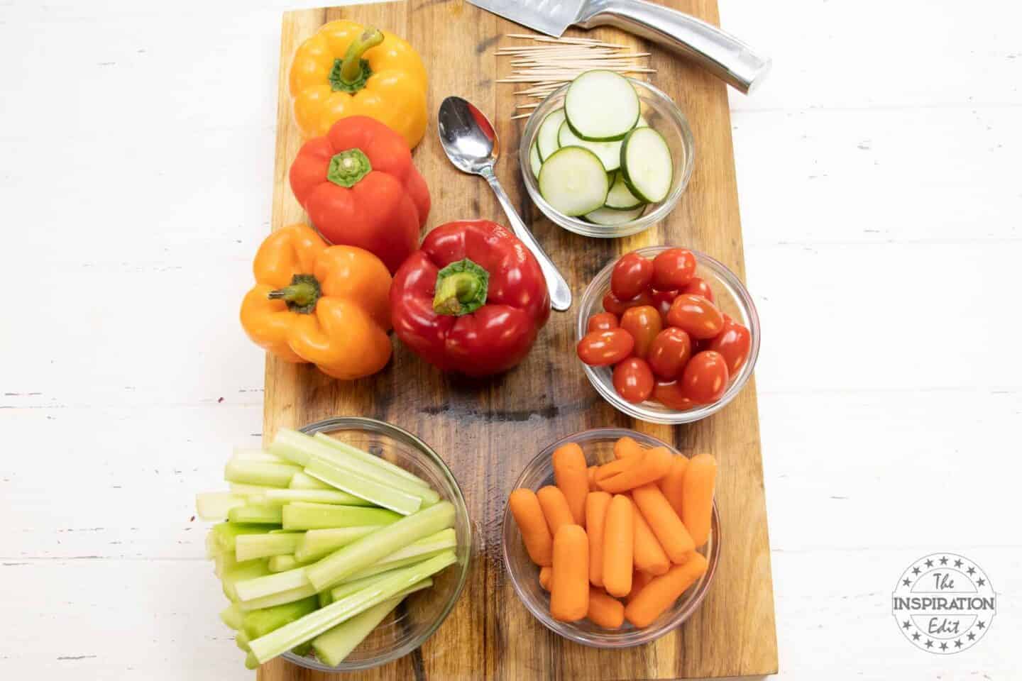 Peppers, cucumbers, tomatoes, carrots and celery cut up on a cutting board.