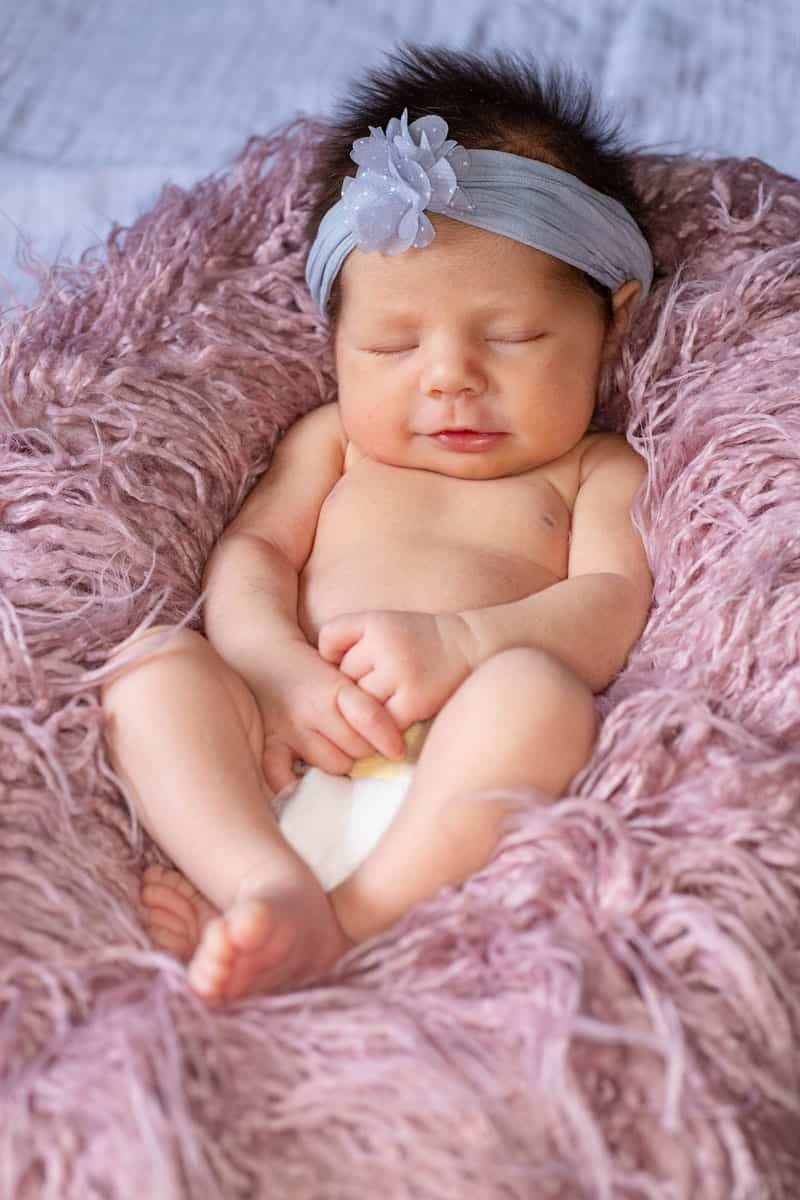 Newborn baby curled up in a pink fuzzy blanket.