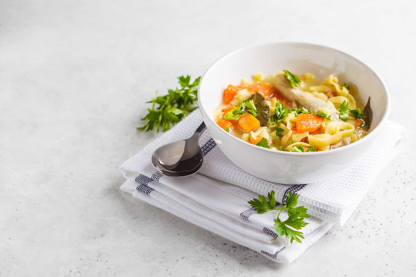 Chicken noodle soup and vegetables in a white bowl on a white background.