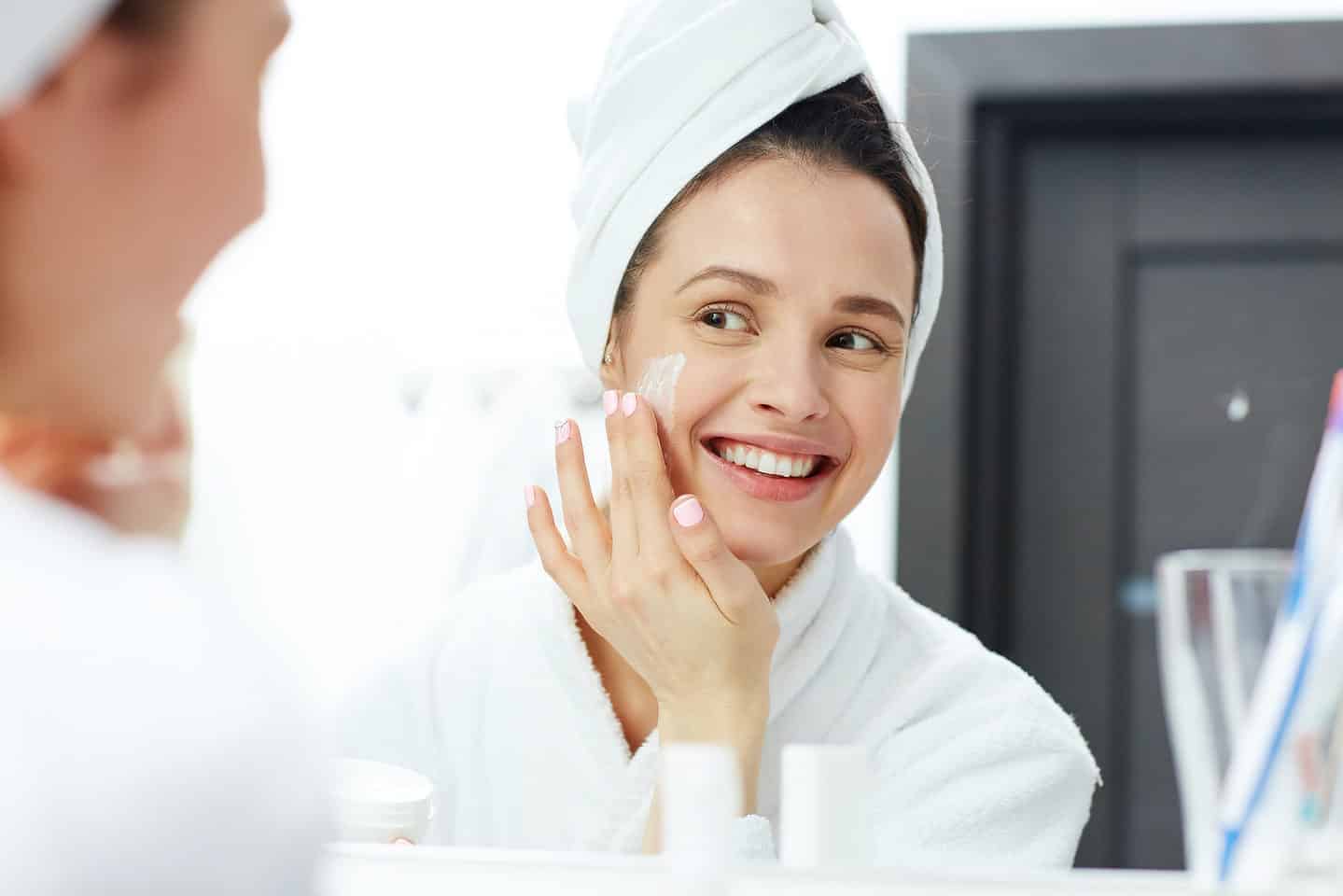 Perfect Young Woman Applying Facial Cream in Bathroom.
