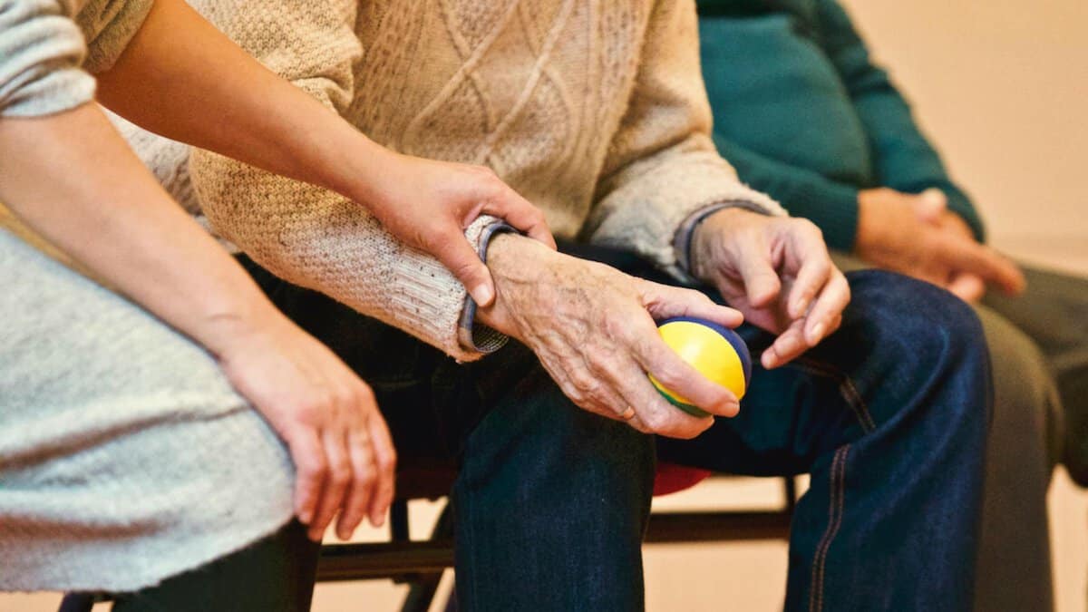 Empathy And Resilience In Caregiving | Helping an old man stead his hand with a ball.