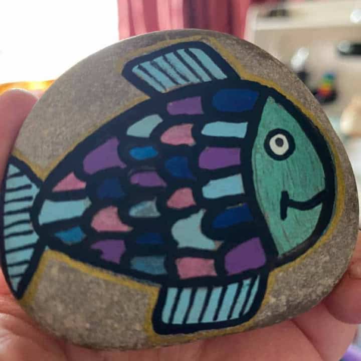 Hand holding a fish painted on a rock.
